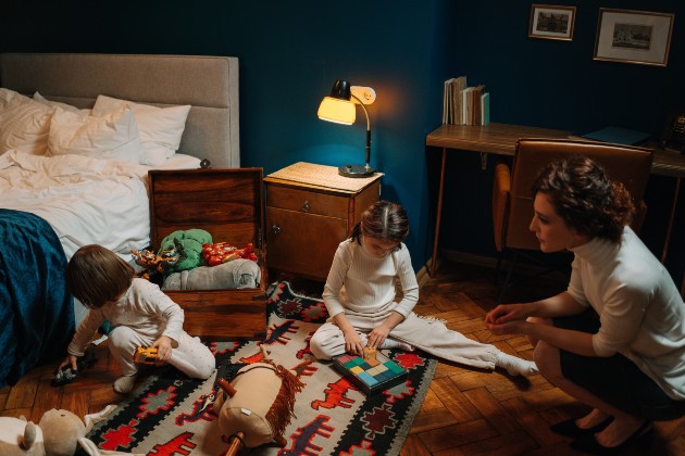 Imagine cu o femeie care se joacă cu doi copii în dormitor