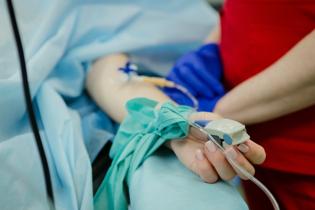 Imagine cu o femeie pe patul de spital, cu o perfuzie în mână