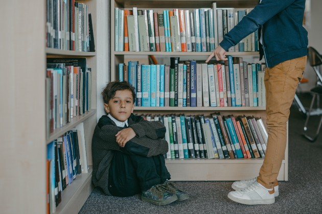 Imagine cu un băiețel care stă în colțul unei biblioteci