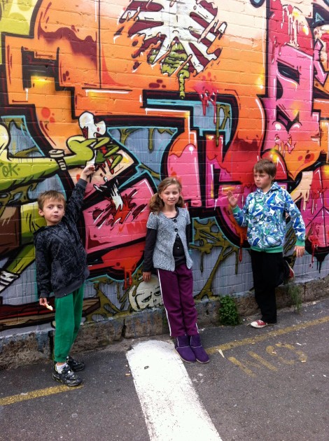 Imagine cu cei trei copii ai lui Rin și Maz lângă un perete desenat