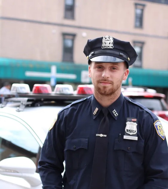 Imagine cu un polițist tânăr lângă mașina de poliție