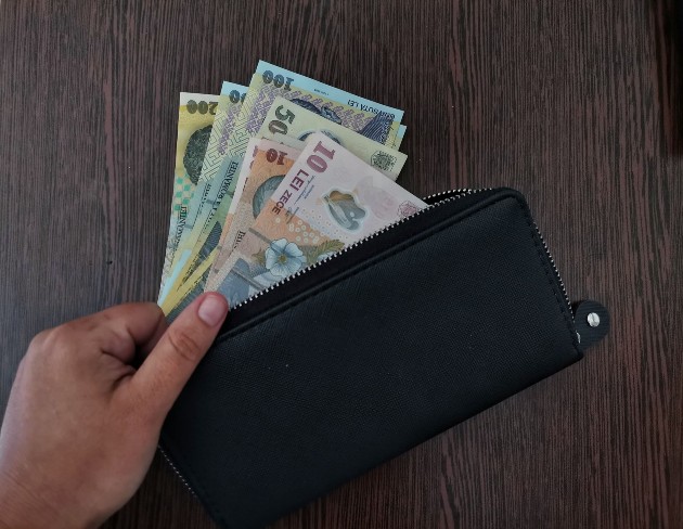 Imagine cu o femeie care ține bani în mână lângă un portofel