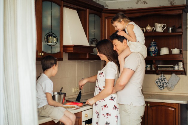 Imagine cu o femeie care gătește, în timp ce copiii și soțul ei stau lângă ea