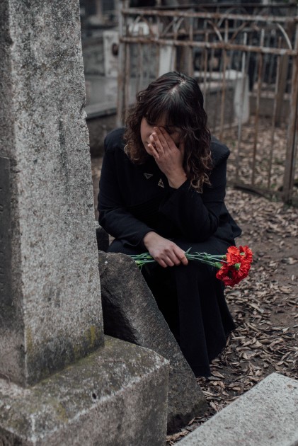 Imagine cu o femeie îmbrăcată în negru care plânge lângă un mormânt