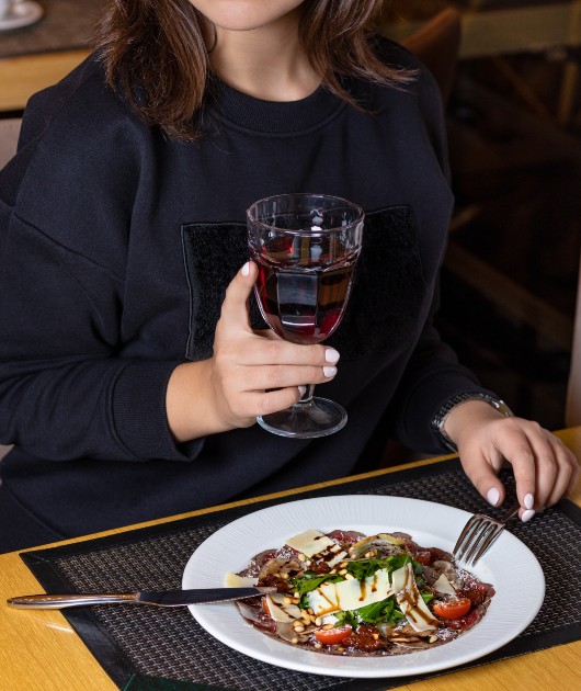 Imagine cu o femeie care mănâncă și ține un pahar de vin în mână