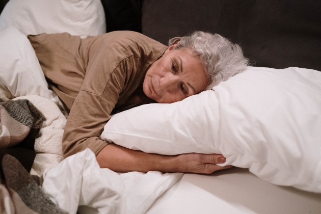 Imagine cu o femeie în vârstă care este tristă și stă în pat