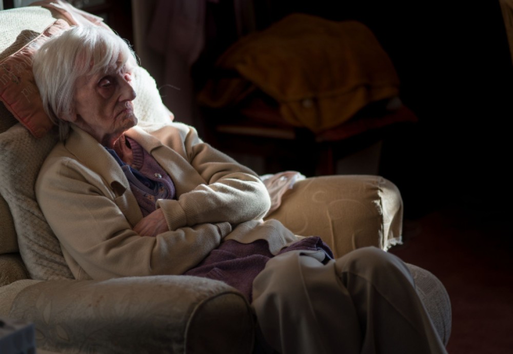 Imagine cu o femeie bătrână tristă care stă întinsă pe pat