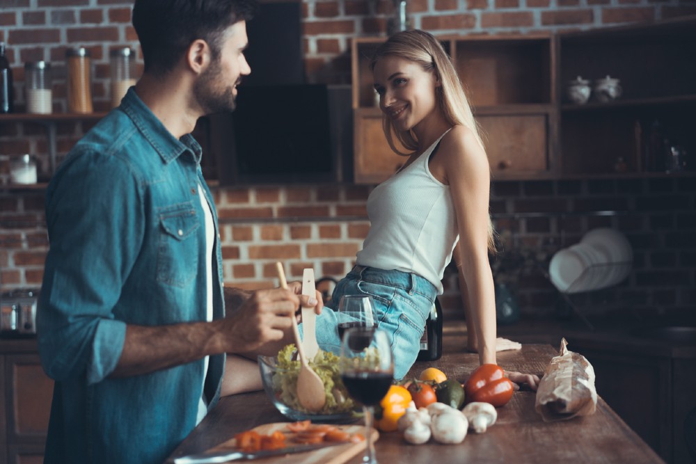 Imagine cu un bărbat care gătește și o femeie care îl admiră