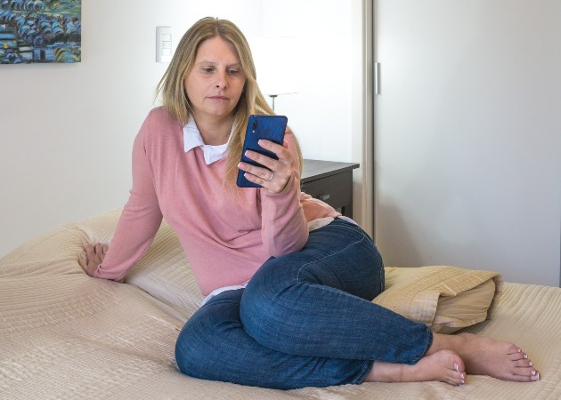 Imagine cu o femeie blondă care stă în pat și se uită la telefon