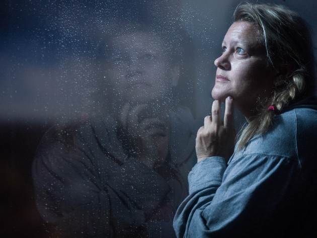 Imagine cu o femeie matură, tristă, care se uită pe geam