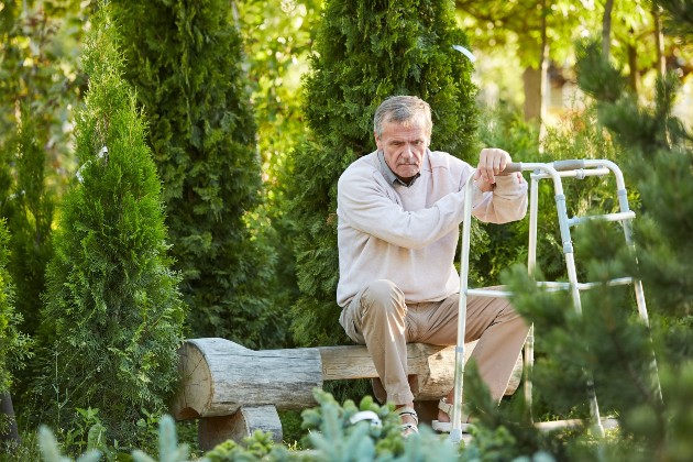 Imagine cu un bărbat bătrân, trist, care stă pe o bancă din lemn