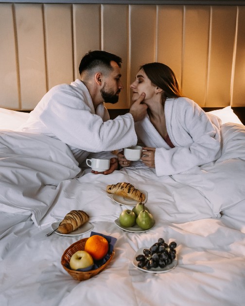 Imagine cu un cuplu care ia micul dejun în pat