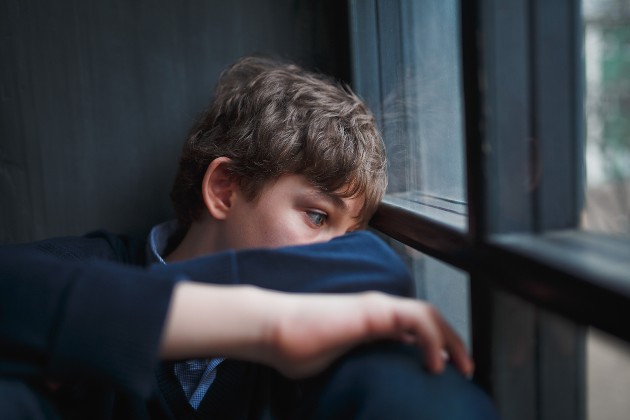 Imagine cu cun băiat trist care se uită pe fereastră