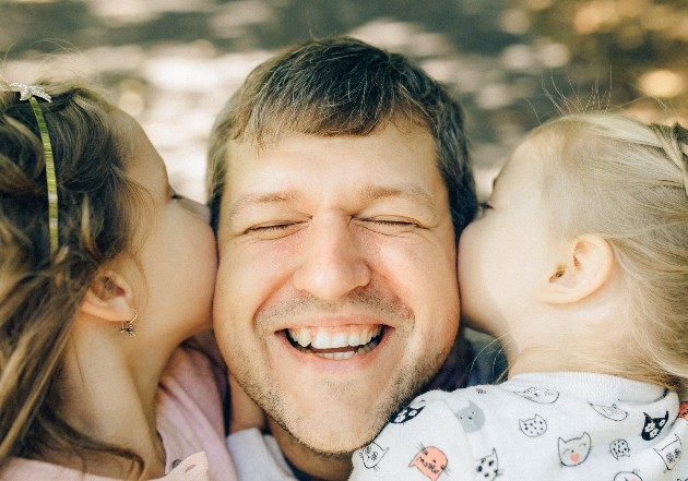 Imagine cu un tătic zâmbitor și cu fiicele sale, care îl îmbrățișează
