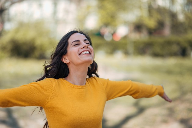 Imagine cu o femeie fericită și liberă, care își întinde mâinile, în parc
