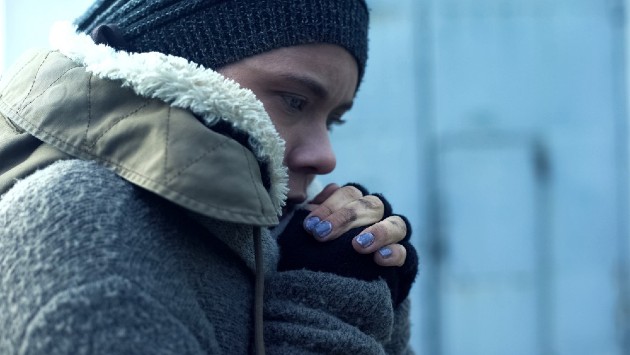 Imagine cu o femeie fără adăpost care își încălzește mâinile