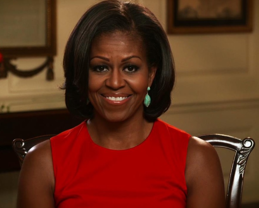 Michelle Obama imbracata intr-o rochie rosie fara maneci, asezata pe scaun