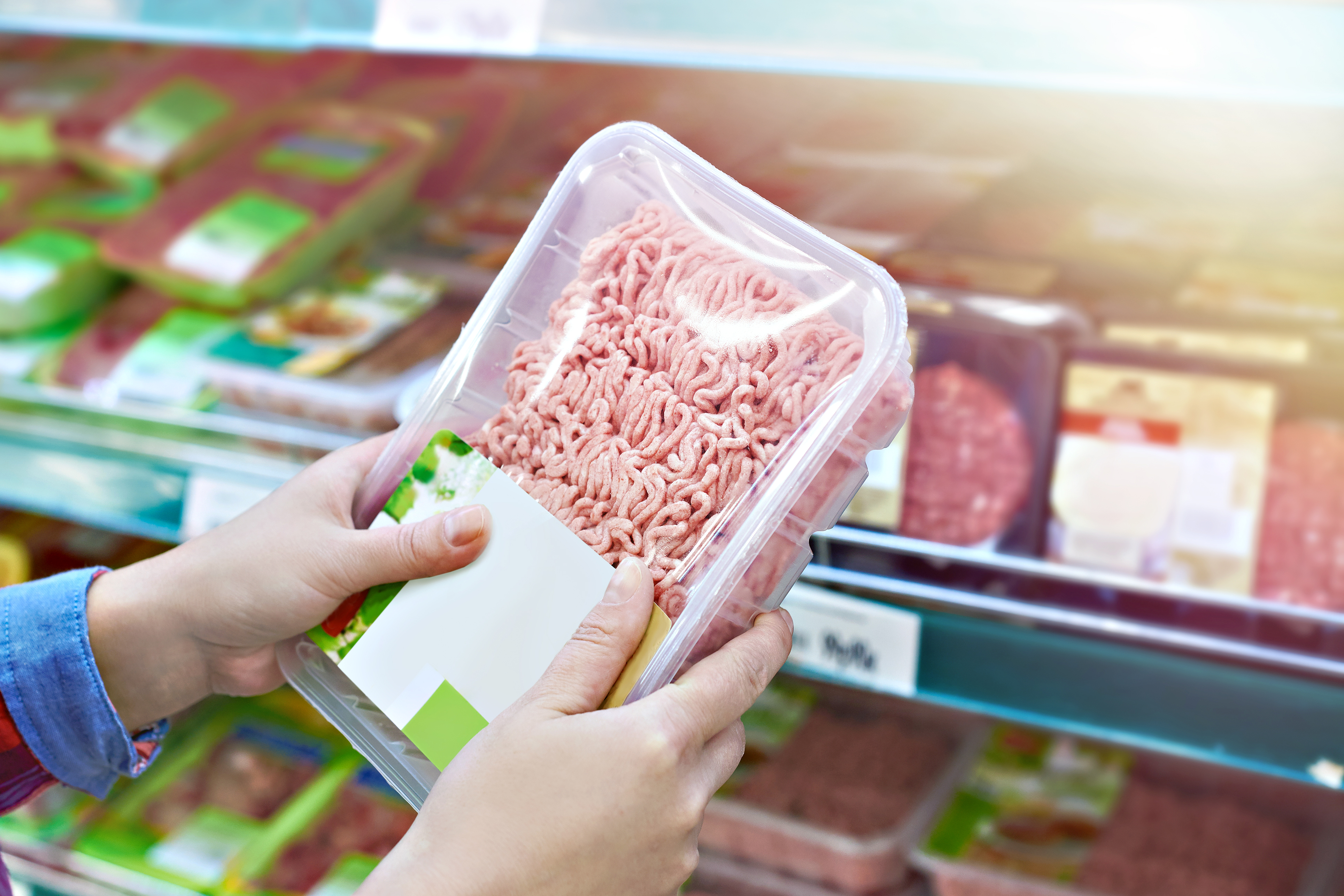 femeie tine in mana o casoleta cu carne tocata intr-un supermarket