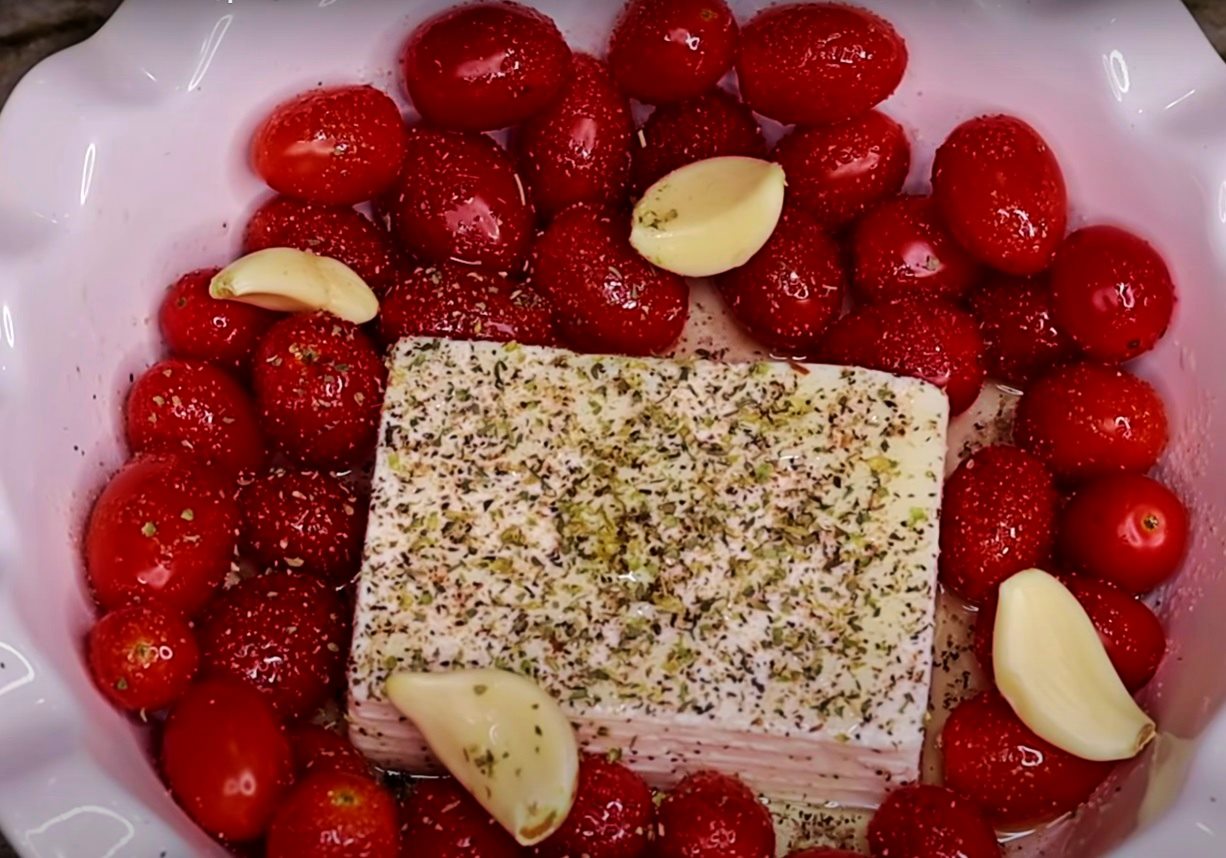 un bol alb cu branza feta in mijloc, rosii cherry si usturoi alaturi