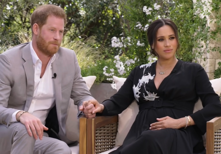 printul harry si meghan markle se tin de mana, stau asezati pe scaun si privesc intr-o parte, in timpul interviului acordat pentru oprah winfrey