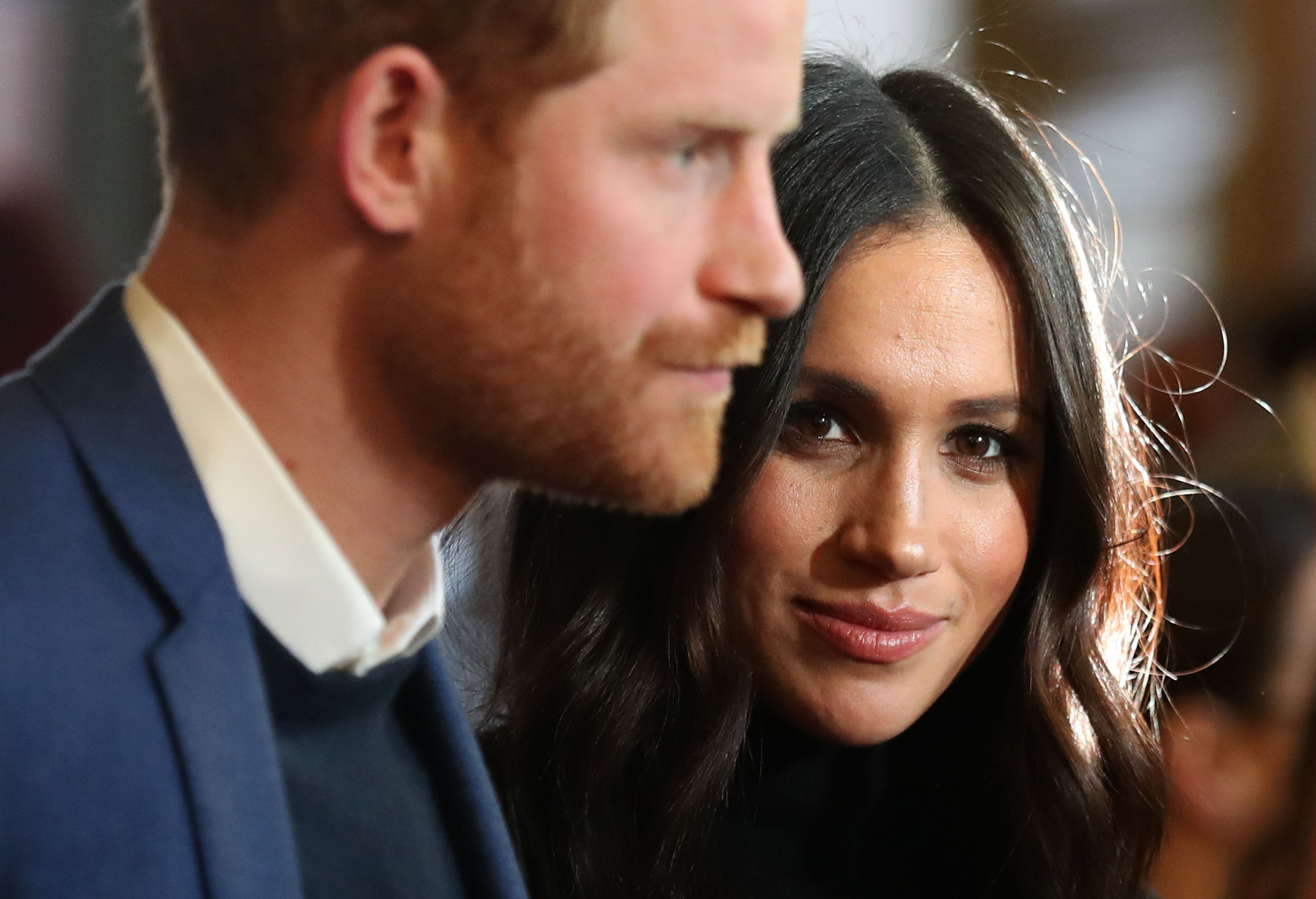 printul harry se uita serios intr-o parte, in timp ce meghan markle priveste fix si zambeste subtil