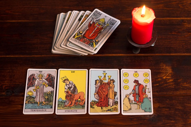 un pachet de carti de tarot langa o lumanare rosie care arde, iar in patru jos patru carti cu simboluri diferite din tarot
