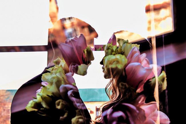 siluete a doi indragostiti care se privesc intens, imagine dublata de un buchet cu flori roz si verzi 
