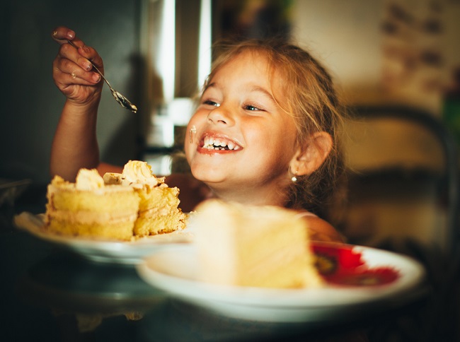 o fetita zambeste larg in timp ce mananca dintr-o felie de tort