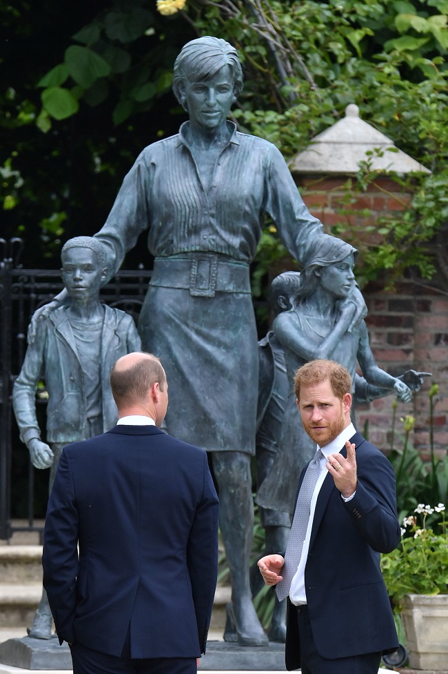 printul william priveste statuia in onoarea printesei diana, in timp ce harry priveste in fata si gesticuleaza