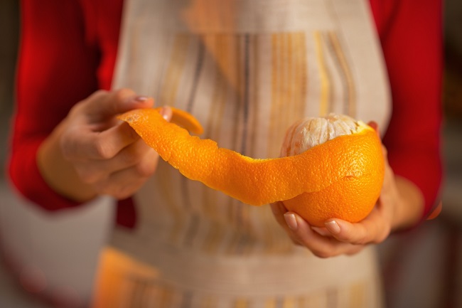 o femeie tine in mana o portocala, pe care o decojeste