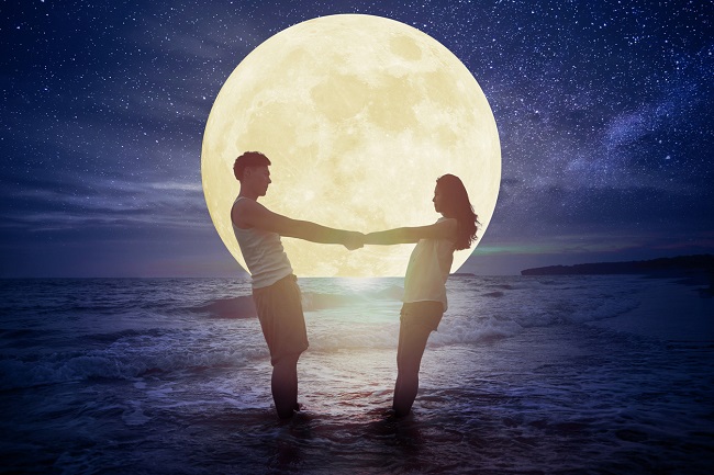 doi indragostiti se tin de mana, in timp ce stau cu picioarele in mare, sub clar de luna