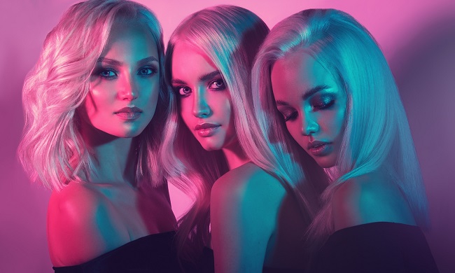 trei femei blonde stau una aproape de cealalta si privesc in parti diferite