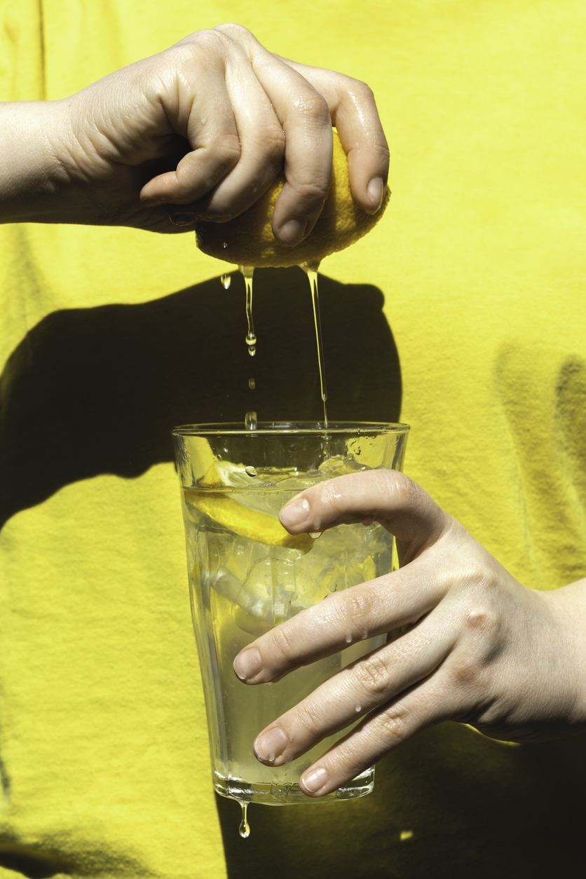 o femeie tine in mana un pahar cu apa si stoarce o jumatate de lamaie