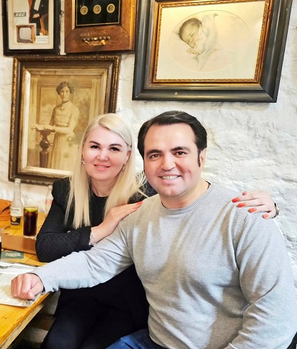 Igor Cuciuc alaturi de sotia lui, Diana, aflati la o masa si cu decor cu tablouri in spate