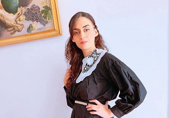 Noemi Troia face poza in rochie neagra cu guler alb de dantela in fata unui tablou pe perete