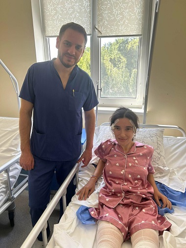 tânără cu picioarele acoperite de bandaje, aflată pe patul de spital în timp ce un cadru medical îi este alături