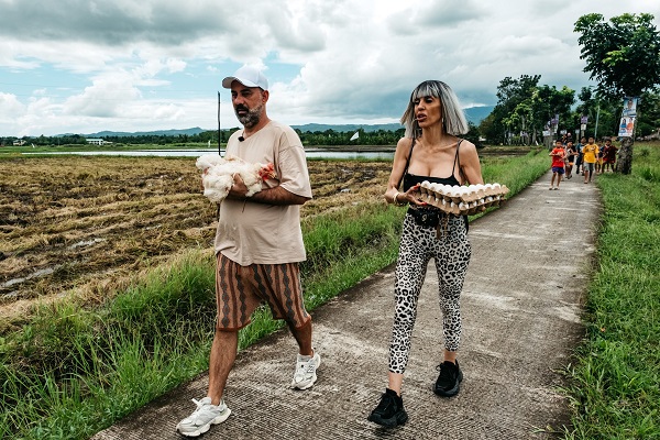 Raluca Bădulescu țin&acirc;nd &icirc;n brațe 2 cartoane de ouă și Florin Stamin țin&acirc;nd &icirc;n brațe o găină &icirc;n timpul competiției Asia Express 2025