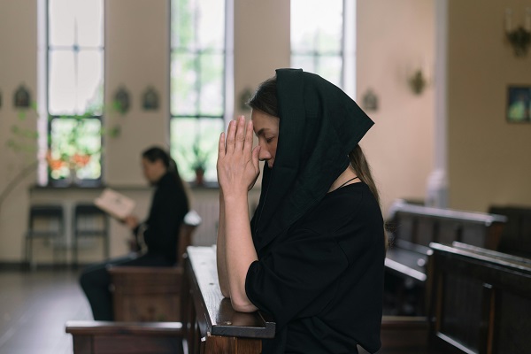 femeie imbracata in negru care se roaga in biserica