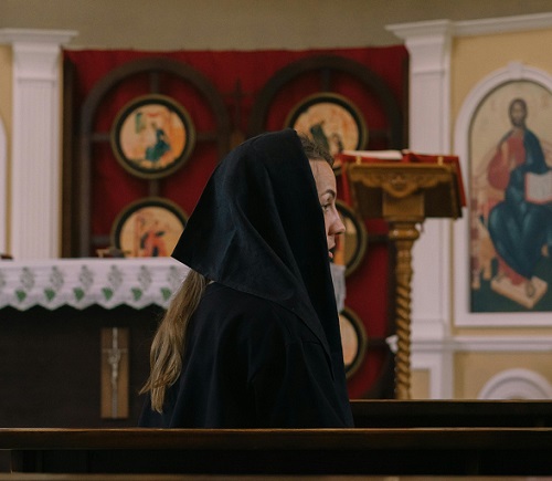 femeie cu basma neagră pe cap stând în biserică