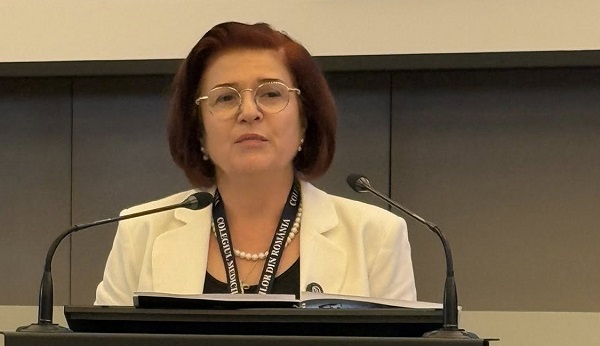 Catalina Poiana, presedintele Colegiului Medicilor din Romania, purtand ochelari, fiind imbracata in sacou alb si bluza neagra, stand la un pupitru cu microfoane in timpul unei sedinte a institutiei pe care o conduce