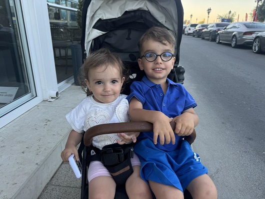 Sara, fetita de 2 ani care a murit la o clinica stomatologica din Bucuresti, imbracata cu bluzita alba si colanti scurti roz, stand alaturi de fratiorul ei cu ochelari in carucior 