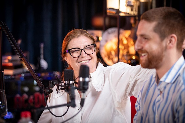 Magda Catone cu ochelari, imbracata in bluza alba, fericita alaturi de fiul ei, Carol, imbracat cu o camasa cu dungi, cand au fost invitati la un podcast