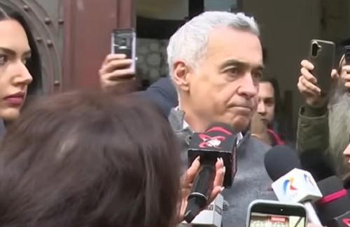 Calin Georgescu imbracat in haina gri, in timp ce se afla la iesirea de la o instanta de judecata si este inconjurat de jurnalisti care ii iau interviu