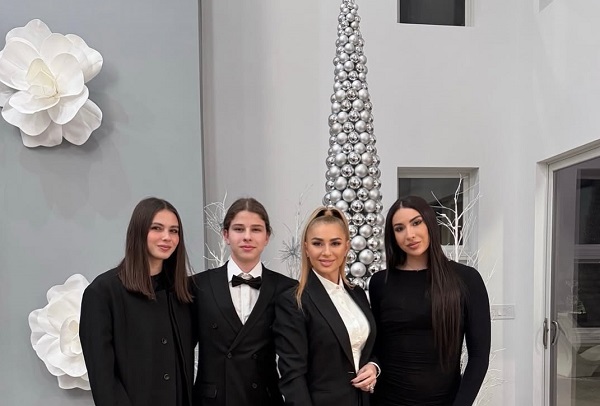 Anamaria Prodan imbracata in costum negru cu camasa alba, fericita alaturi de cei trei copii ai ei, Laurentiu Jr, Sarah si Rebecca, toti trei imbracati in negru, langa un brad de Craciun din globuri argintii