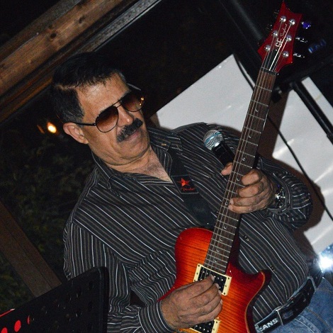 Dan Ciotoi imbracat cu camasa neagra cu dulgi albe si blugi, purtand ochelari negri in timp ce canta la chitara intr-un program artistic de la un restaurant