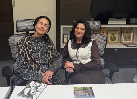 Sofia Vicoveanca imbracata cu un pulover gri inchis cu alb, avand pe cap si pe umeri o esarfa cu imprimeu animal print, stand zambitoare pe scaun alaturi de Larisa Blanari, managerul Spitalului Clinic Județean de Urgență Suceava, imbracata in maro, cu o vesta alba, stand amandoua intr-un birou in care se afla icoane si un televizor