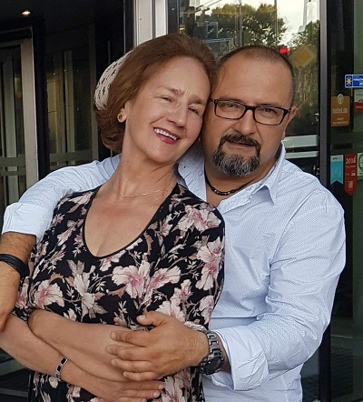 Sofia Vicoveanca fericita, imbracata cu o bluza neagra cu maneca lunga cu imprimeu cu flori mari roz, in timp ce este imbratisata de fiul ei, Vlad, imbracat cu camasa alba, stand amandoi in fata unui hotel