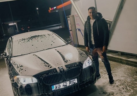 Madalin Ionut Geamanu, tanarul care a murit in accidentul de la Calimanesti, imbracat cu geaca neagra si blugi, stand langa masina sa plina de spuma la o spalatorie 