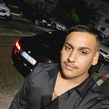 Madalin Ionut Geamanu, tanarul de 19 ani care a murit in accidentul de la Calimanesti, imbracat in negru, stand langa masina sa BMW intr-o parcare de pe langa niste blocuri dintr-un oras