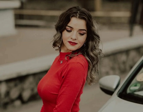 Corina Matraș, tanara de 26 de ani decedata intr-un accident rutier, imbracata in rosu, cu privirea in jos, in timp ce statea langa o masina